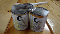 Two cans of Moon Valley Kushgard Linseed Sealer and Varnish on a wooden surface with a brush.